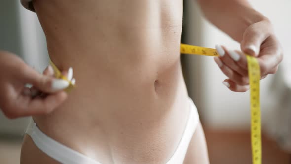 A Girl is Measuring Her Waist with a Centimeter Tape