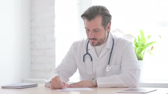 Young Doctor Writing on Paper in Clinic Medical Report