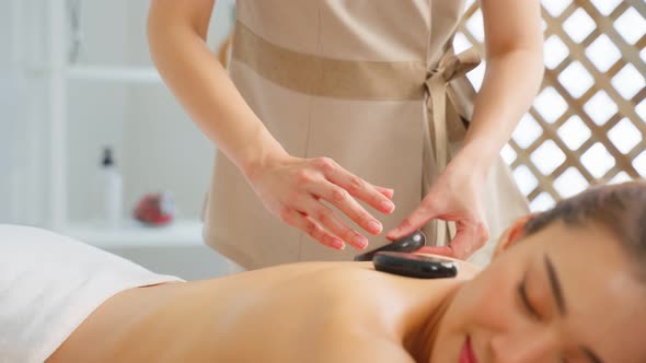 Asian young relaxing woman getting back massage therapy with hot stone in spa beauty salon