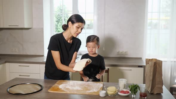 Mother Shows Pretty Girl How to Toss Up Thin Elastic Dough