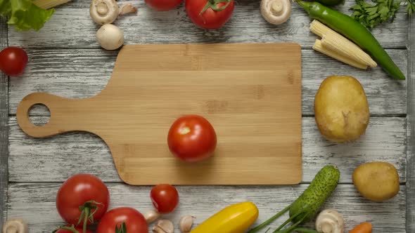 A Male Hand Spins a Red Tomato on a Wooden Cutting Board