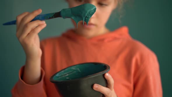 Closeup of a Brush and a Bowl of Blue Paint Against a Portrait of a Teenage Girl in an Orange