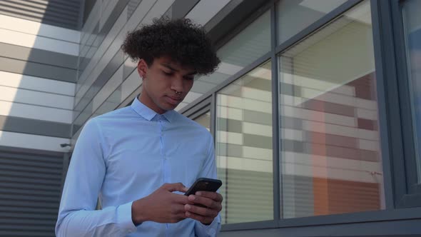 Well Dressed Business Guy Walks Near the Building with a Smartphone