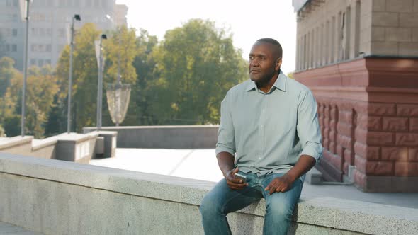 Adult Mature African American Man Sitting Outdoors Holding Smartphone Looking at Screen Greeting