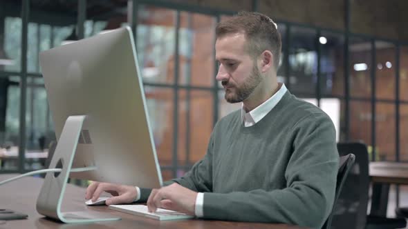 Young Man Working on Computer and Smiling at Camera