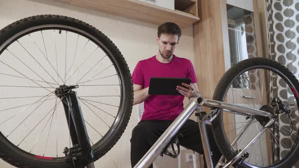 Man Sits Near Disassembled Bicycle with Tablet Tries to Figure Out Breakdown