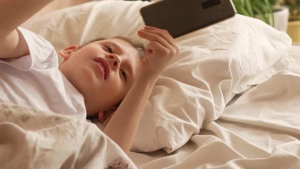 Caucasian boy lying in bed wakes up from the alarm clock, continues to sleep.