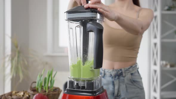 Young Unrecognizable Woman Mixing Green Healthful Detox Vegan Cocktail in Blender at Home