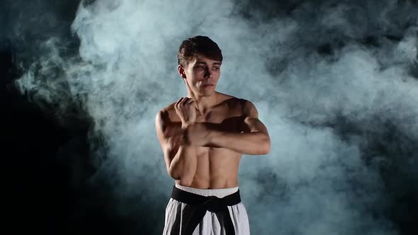 Man Training Taekwondo or Karate with a Naked Torso and a Black Belt, Smoke, Slow Motion