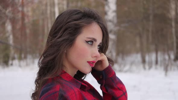 Young Woman with Wavy Hair Standing and Touching Face in Winter Forest