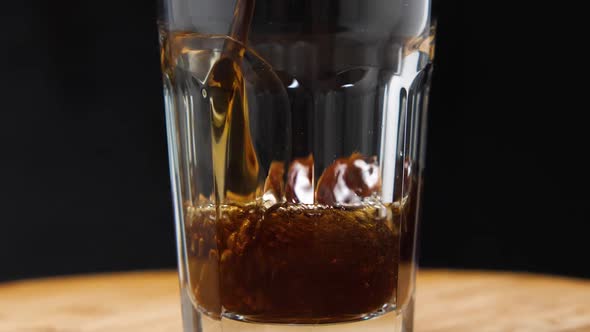 A close-up of a dark carbonated drink being poured into a glass