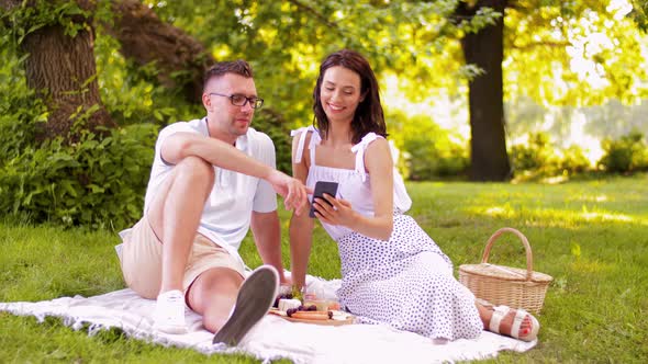 Happy Couple with Smartphone at Picnic in Park