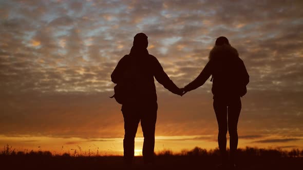 Silhouettes of Two Hikers with Backpacks Enjoying Sunset View From Top of a Mountain