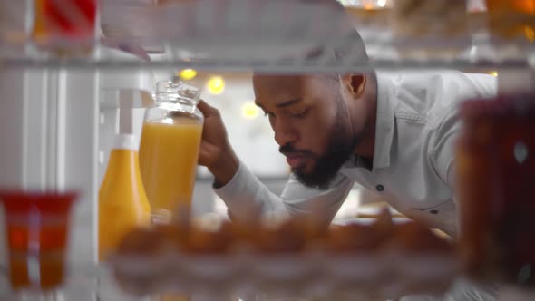 View From Inside Fridge of African Man Opening Door and Pouring Glass of Cool Orange Juice