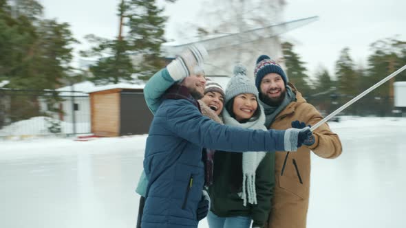 Happy Men and Women Holding Smartphone with Selfie Stick and Taking Photos in Ice-skating Rink