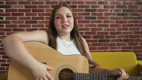 Young Woman with an Acoustic Guitar in Her Hands Explains Its Structure and How to Play Front View