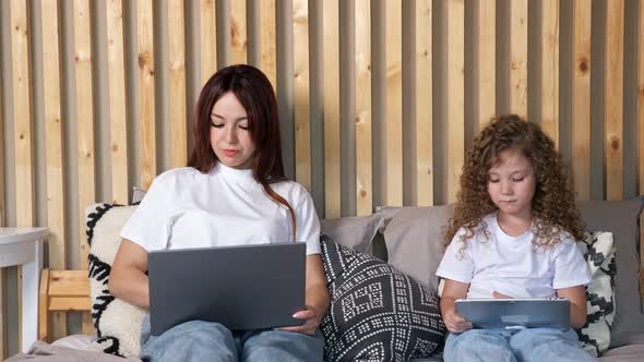 Concentrated Woman with Laptop and Daughter with Tablet