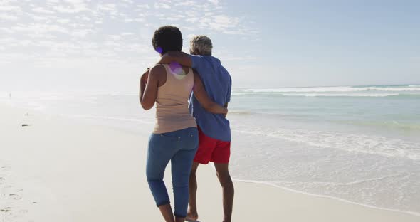 Happy african american couple walking and embracing on sunny beach