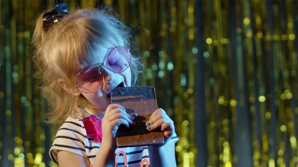 Stylish Trendy Young Child Girl at Disco Party Cyberpunk Club Eating Big Chocolate Bar Sweet Candy