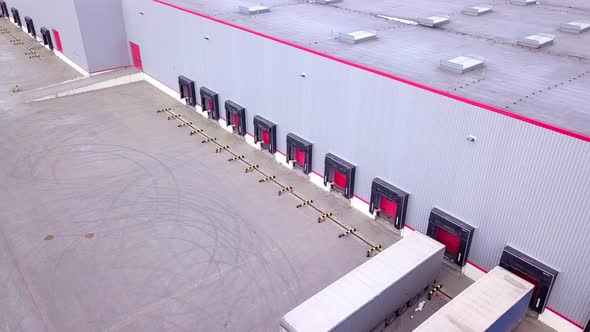 Moving Aerial Side Shot of Industrial Warehouse Loading Dock where Many Truck with Semi Trailers Loa