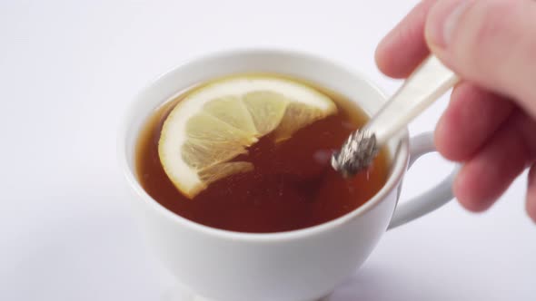 hand adds cane sugar with a dessert spoon in a cup with hot black tea and with a slice of lemon 