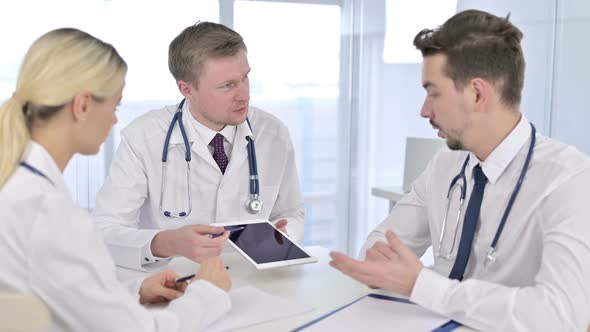 Serious Male Doctor Discussing Reports on Tablet with Team in Office