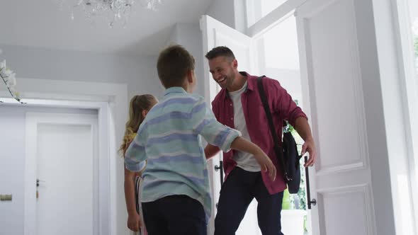 Excited caucasian son and daughter at home running and hugging father coming through the front door