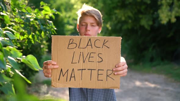 a Young Caucasian Teenager in a Blue Shirt Holds a Cardboard Box with Handwritten Text BLACK LIVES