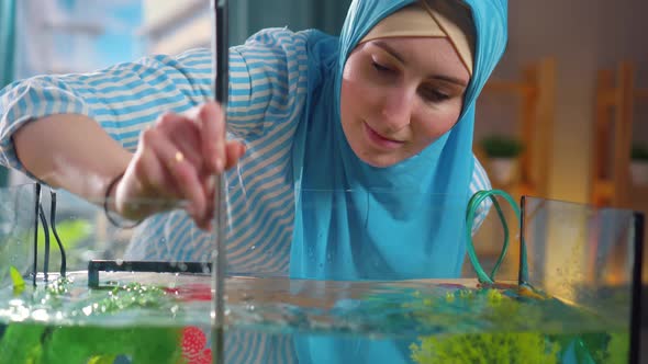 Close Up Muslim Woman in National Headscarf Cleans Aquarium with Sponge