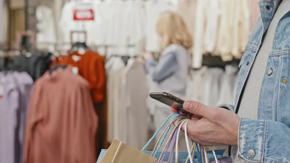 Man With Smartphone During Clothes Shopping With Girlfriend