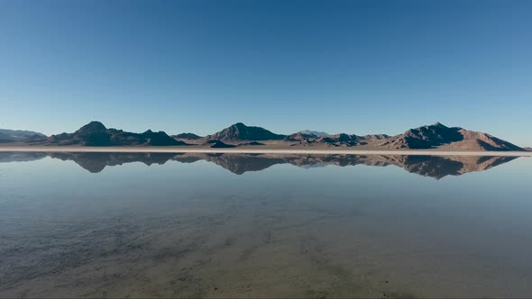 An aerial drone shot reveals smooth water covering the Bonneville Salt Flats and reflects the distan