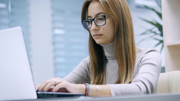 Cute Young Girl Working at a Laptop with Glasses Typing Text in the Office Employee at Work on the