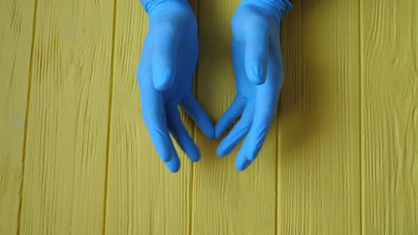 Doctor Male Hands in Blue Sterile Glove Against a Yellow Wooden Table Background