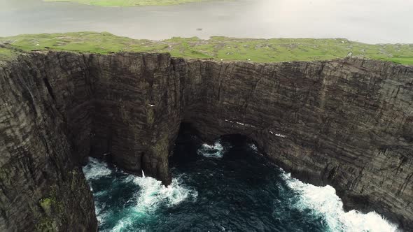 Aerial view of bird flying around foggy English Slave cliff, Faroe island.