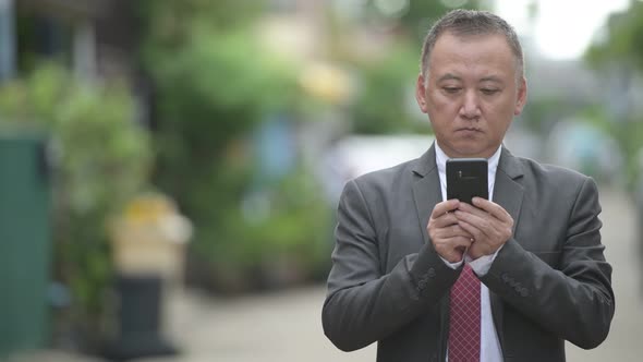 Mature Japanese Businessman Using Phone in the Streets Outdoors