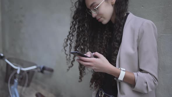 CurlyHaired Moroccan Lady Smiling While Looking On Her Smartphone