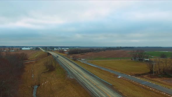 Cars, trucks and a bus traveling across an overpass running over railroad tracks next to a pond on a