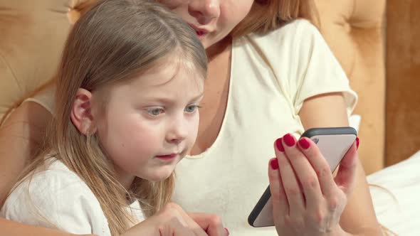 Adorable Little Girl Using Smart Phone with Her Mother