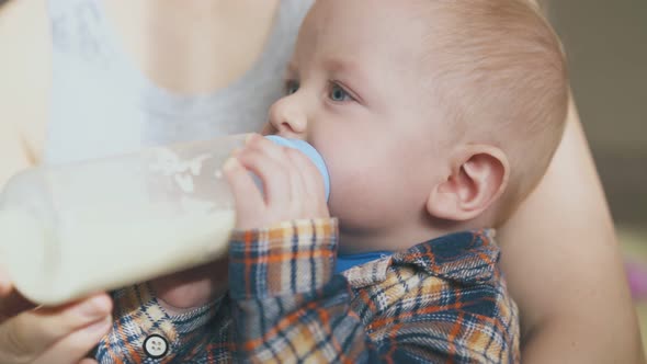 Lovely Boy Eats Food From Bottle in Mother Arms Closeup