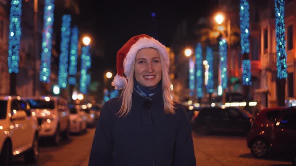 A beautiful woman in a Santa Claus hat walks at night on Christmas