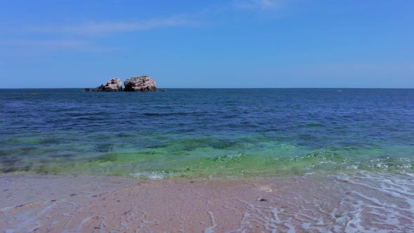 Sunny Beach with Blue Sea Water, Blue Sky and Rocks on the Horizon in a Summer Day. Wide shot