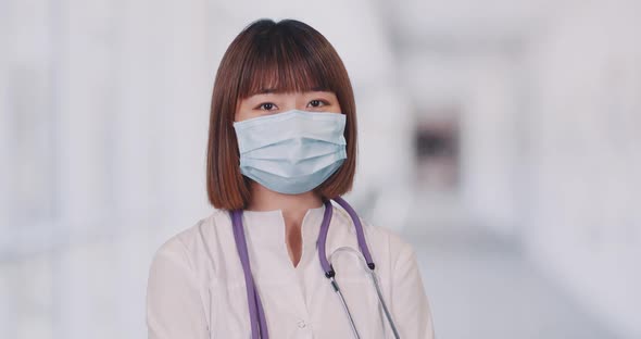 Portrait of Young Asian Female Doctor, Woman in Medical Mask Looks at the Camera, White Blurred