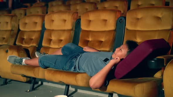 A Boy Laying Down on Armchair in Cinema