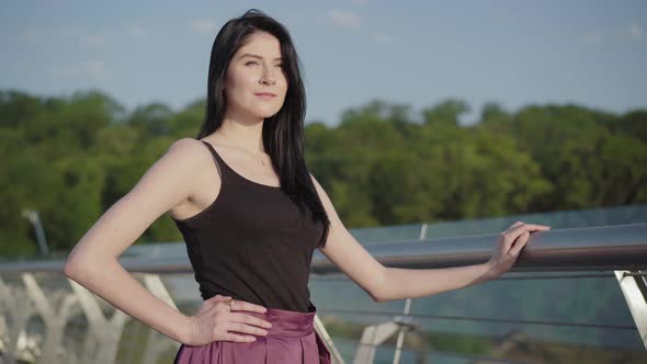 Portrait of Confident Beautiful Caucasian Woman Standing on Bridge on Sunrise and Smiling. Charming