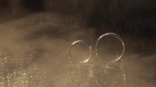 Wedding Rings on Dark Water Surface Shining with Light. Water Drops. Close Up