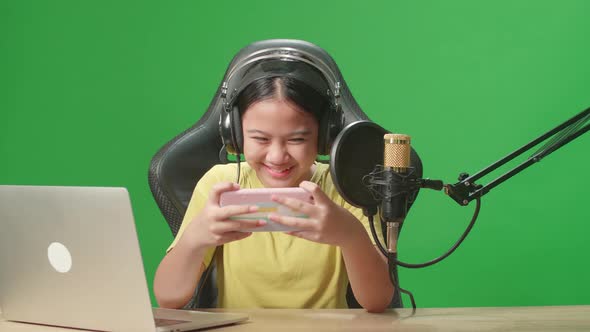 Excited Asian Kid Girl Playing Video Game With Mobile Phone While Live Stream On Green Screen