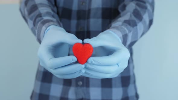 Hands in protective medical rubber gloves are showing little red heart present for Valentine's Day