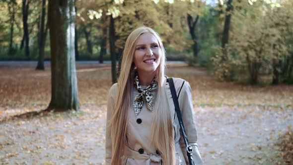 Beautiful Young Blonde Girl Walking in the Park in Autumn and Smiling