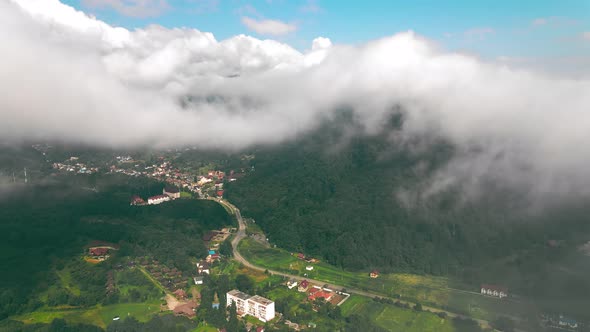 Aerial View Flight Over the Clouds Through Which You Can See the Village Between the Mountains. View