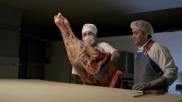 Worker in Mask Moves Suspended Beef Carcass and Put on Slaughterhouse Table at Meat Processing Plant